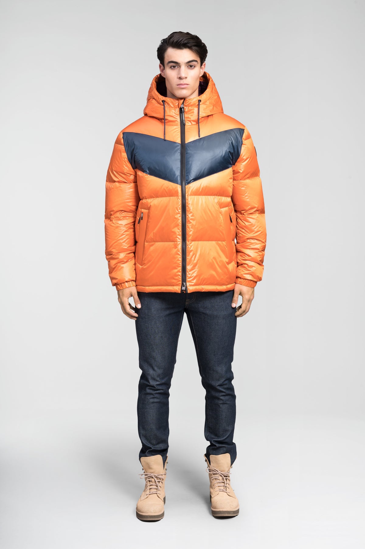 Dyna Men's Chevron Quilted Puffer Jacket in hip length, premium cire technical nylon taffeta fabrication, Premium Canadian origin White Duck Down insulation, non-removable down-filled hood, two-way centre-front zipper, fleece-lined zipper pockets at waist, pit zipper vents, in Burnt Orange