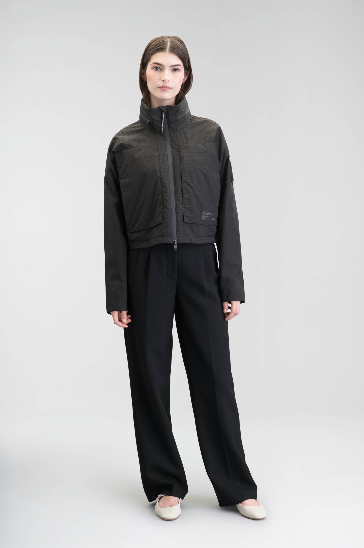 Epsie Women's Cropped Rain Jacket in Black crafted from premium recycled polyester ripstop with a DWR coating and taffeta nylon lining. Features a hidden packaway hood stored in the collar, two-way waterproof front zipper, seam-sealed construction, underarm zip ventilation, adjustable drawcord hem, zippered waist patch pockets, and an interior chest pocket for secure storage. Machine washable. Designed in Canada.