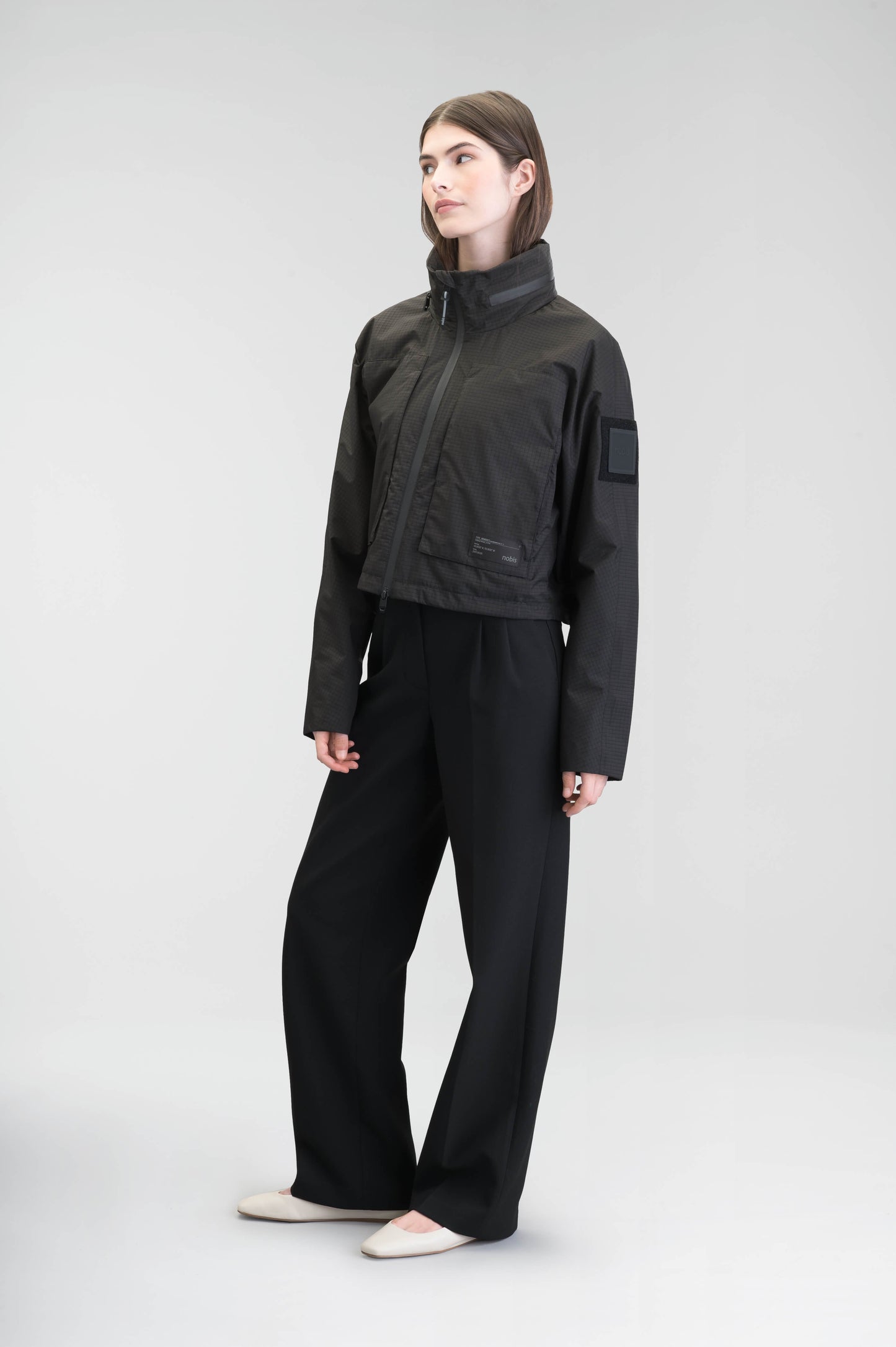 Epsie Women's Cropped Rain Jacket in Black crafted from premium recycled polyester ripstop with a DWR coating and taffeta nylon lining. Features a hidden packaway hood stored in the collar, two-way waterproof front zipper, seam-sealed construction, underarm zip ventilation, adjustable drawcord hem, zippered waist patch pockets, and an interior chest pocket for secure storage. Machine washable. Designed in Canada.