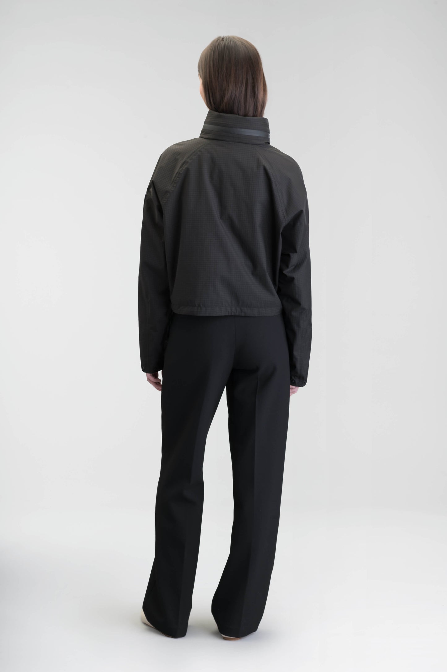 Epsie Women's Cropped Rain Jacket in Black crafted from premium recycled polyester ripstop with a DWR coating and taffeta nylon lining. Features a hidden packaway hood stored in the collar, two-way waterproof front zipper, seam-sealed construction, underarm zip ventilation, adjustable drawcord hem, zippered waist patch pockets, and an interior chest pocket for secure storage. Machine washable. Designed in Canada.