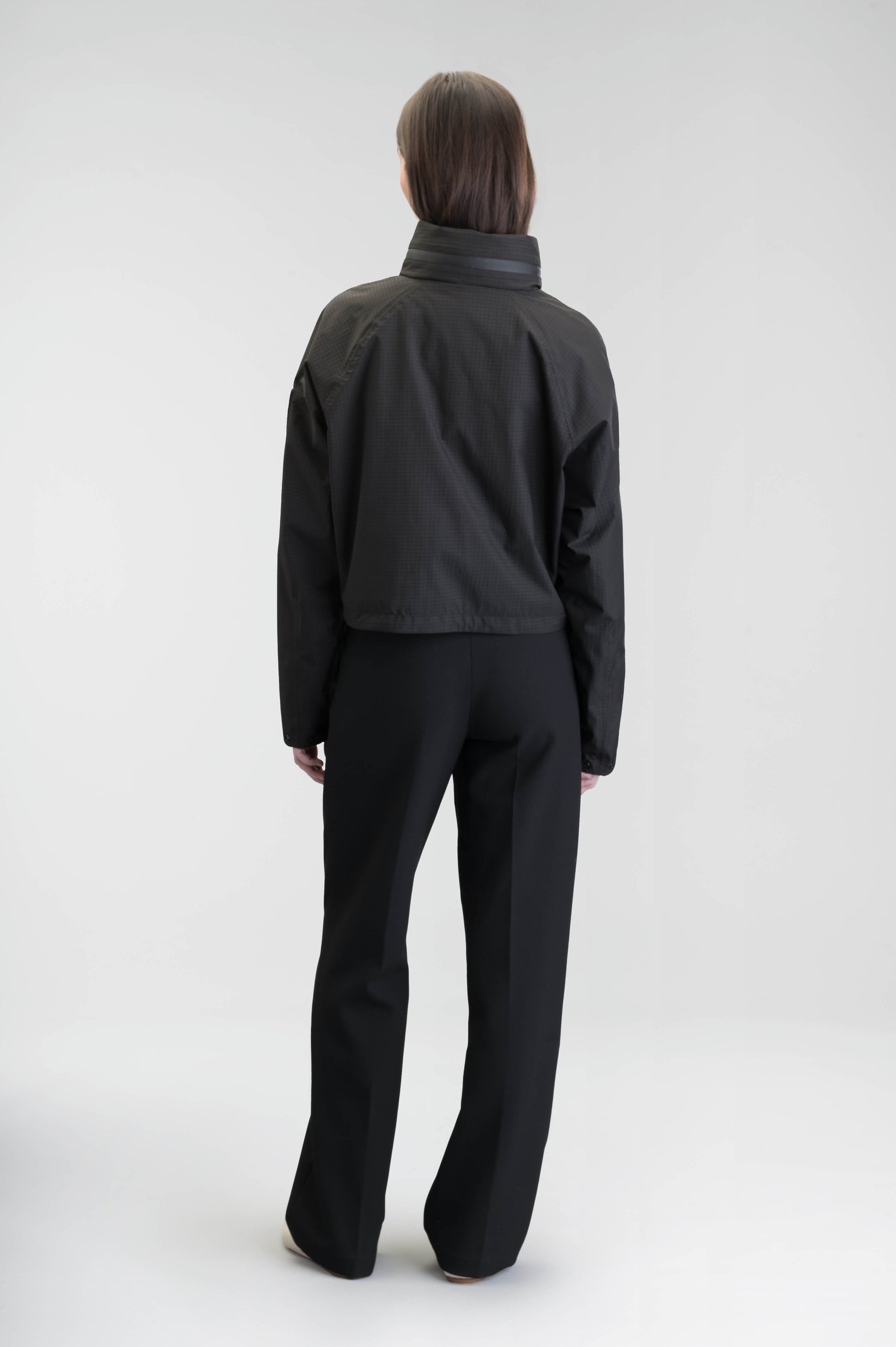 Epsie Women's Cropped Rain Jacket in Black crafted from premium recycled polyester ripstop with a DWR coating and taffeta nylon lining. Features a hidden packaway hood stored in the collar, two-way waterproof front zipper, seam-sealed construction, underarm zip ventilation, adjustable drawcord hem, zippered waist patch pockets, and an interior chest pocket for secure storage. Machine washable. Designed in Canada.
