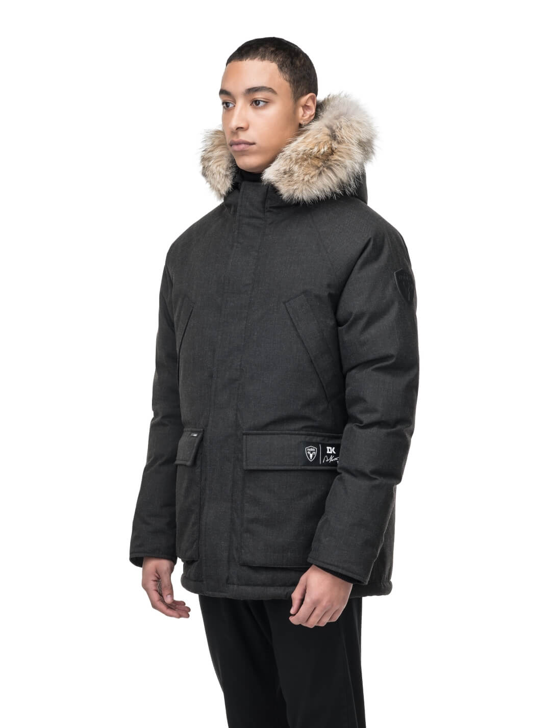 Duncan Keith Heritage Men's Parka in hip length, and features Canadian duck down insulation, non-removable hood with removable coyote fur trim, fleece-lined chest pockets, top and side entry waist pockets, adjustable waist cord, interior zipper pocket, and co-branding with Keith's signature on the left outer waist pocket, in H. Black