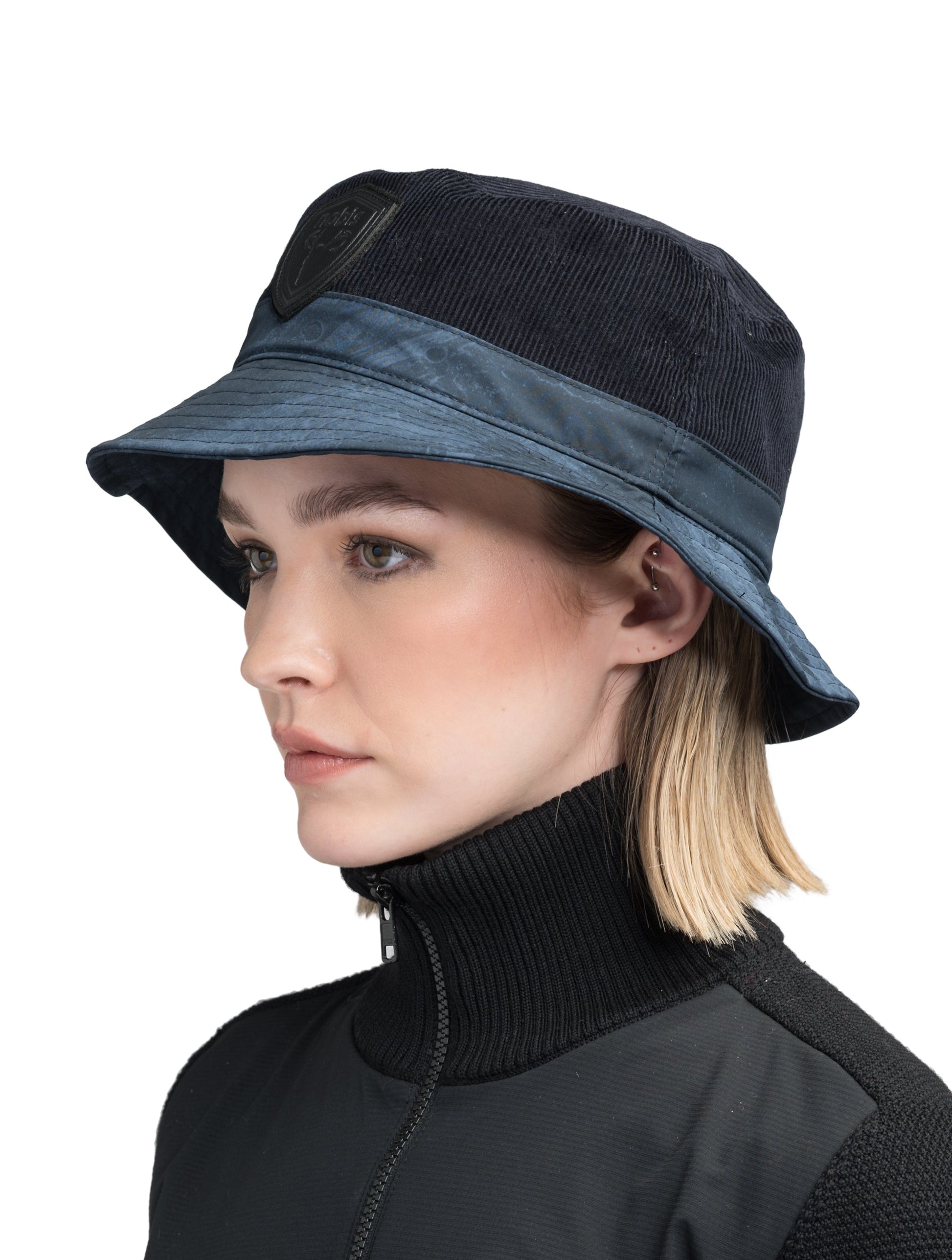 Kaia Unisex Tailored Bucket Hat in a 100% cotton corduroy and 3-ply micro denier fabrication, unstructured crown, black leather Nobis shield logo on crown front, and small flap pocket on the right side crown, in Navy