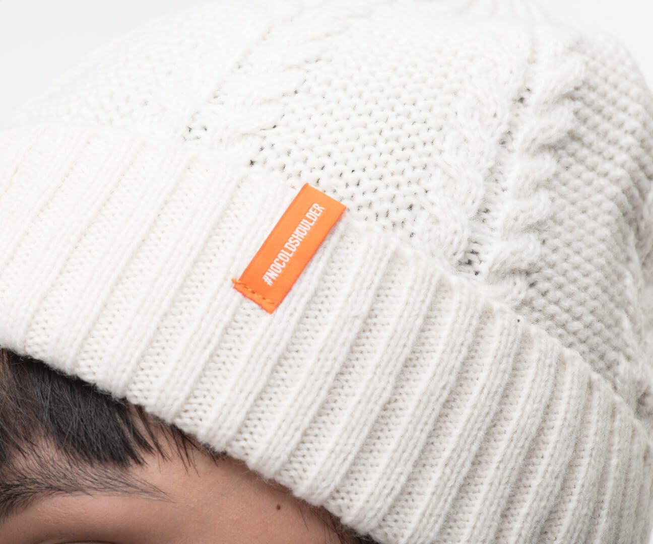 No Cold Shoulder unisex beanie with cable stitched crown, two by two rib knit cuff, with dual orange wrap labels along cuff, in Chalk